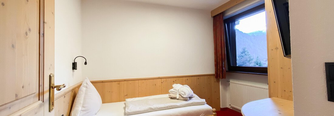 Ein einfaches Schlafzimmer mit Holzverkleidung und rotem Teppich. Es gibt ein Bett, einen Tisch und ein Fenster mit Aussicht. - Hotel Stern - Längenfeld