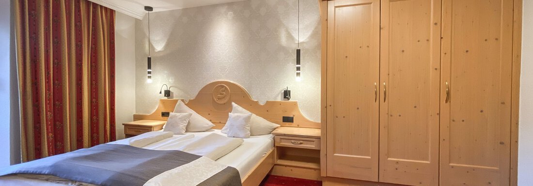 Ein gemütliches Schlafzimmer mit einem Doppelbett und stilvollen Holzmöbeln. Die Wände sind in neutralen Tönen gehalten und das Zimmer ist gut beleuchtet. - Hotel Stern - Längenfeld