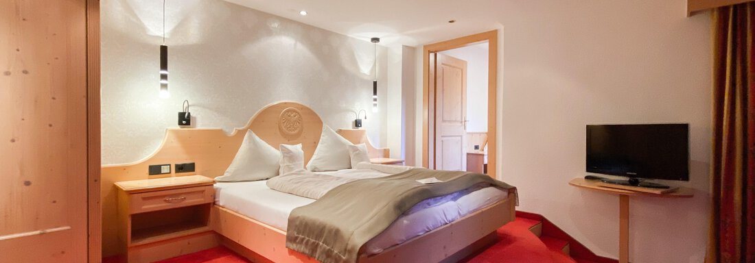Ein modernes Schlafzimmer mit einem großen Bett und hellem Holzinterieur. Der Raum ist mit einem Fernseher und einem gemütlichen Teppich ausgestattet. - Hotel Stern - Längenfeld