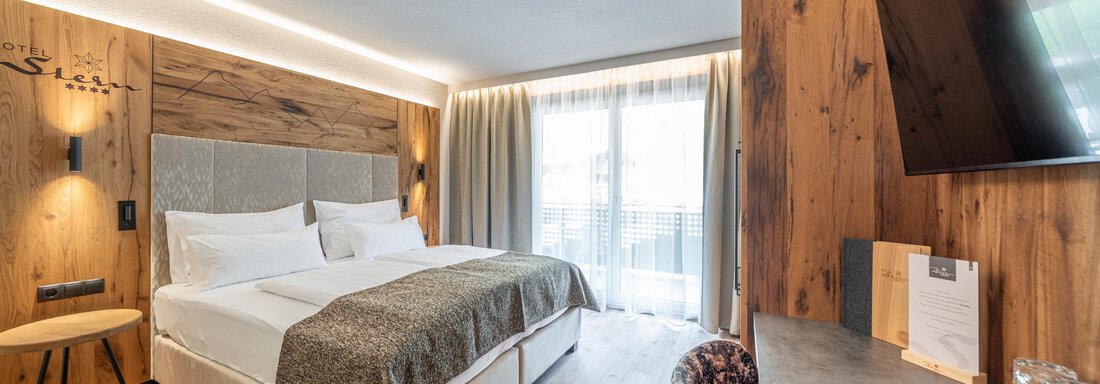 web-stern-zimmer-211-1010 Ein modernes Hotelzimmer mit einem großen Doppelbett und einer gemütlichen Sitzgelegenheit. Große Fenster sorgen für viel Tageslicht. - Hotel Stern - Längenfeld