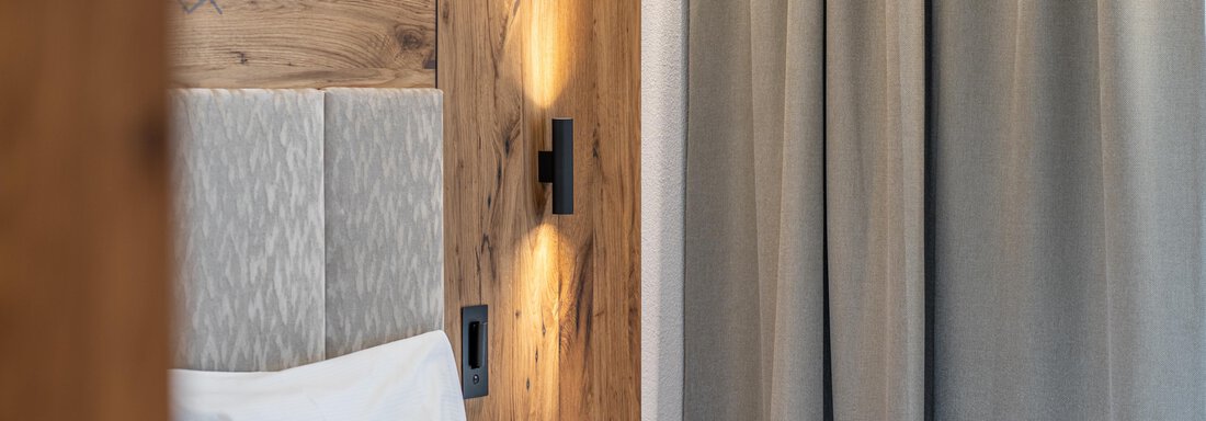 Ein modernes Schlafzimmer mit einem Kopfteil aus Holz und weißen Kissen. Die Vorhänge sind grau und sorgen für eine gemütliche Atmosphäre. - Hotel Stern - Längenfeld
