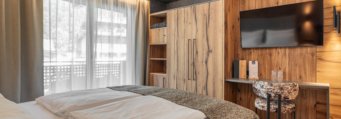Ein modernes Zimmer mit einem komfortablen Bett und holzverkleideten Wänden. Große Fenster sorgen für viel Tageslicht und eine gemütliche Atmosphäre. - Hotel Stern - Längenfeld