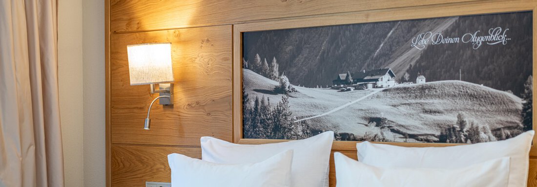 Ein modernes Schlafzimmer mit einem Holzpaneel und einem großen Bild einer Landschaft. Es gibt zwei große Kissen auf dem Bett und eine sanfte Wandbeleuchtung. - Hotel Stern - Längenfeld