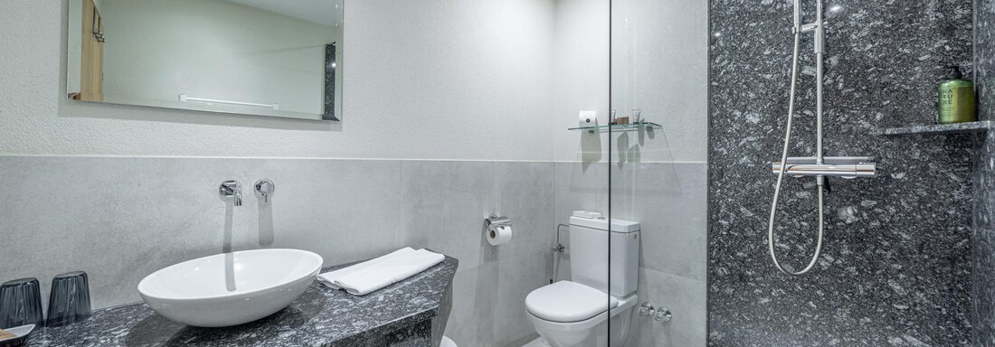 Ein modernes Badezimmer mit einer walk-in Dusche und eleganten Steinelementen. Die Ausstattung umfasst ein Waschbecken und eine schlichte Toilette. - Hotel Stern - Längenfeld