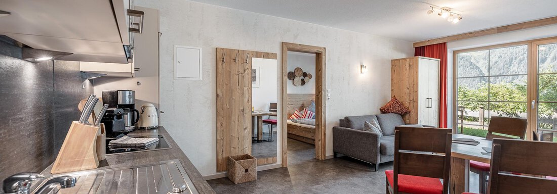 Apartement1_Himmelreich_MyAlps_byRudiWyhlidal-3295 A modern kitchen with an open living area features a dining table and a cozy sofa. Large windows let in plenty of light and offer a view outside. - MYALPS Himmelreich - Längenfeld