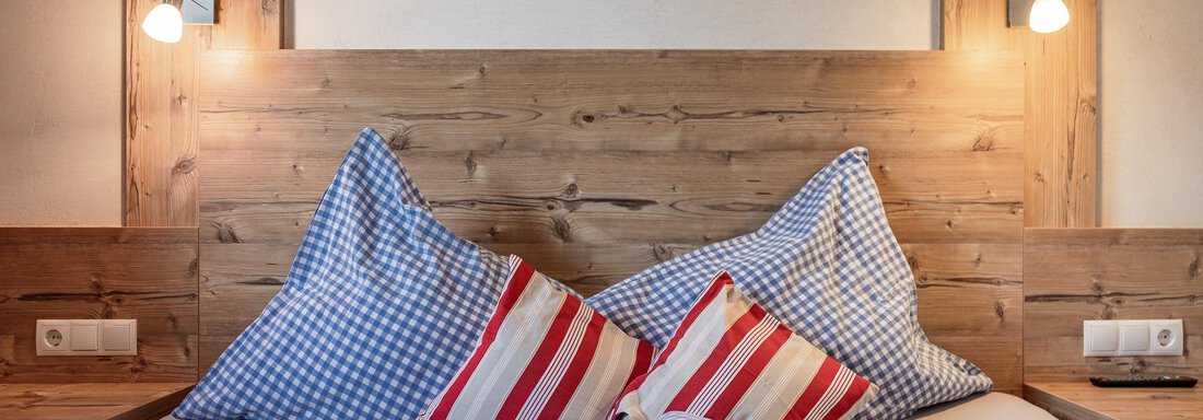 A cozy bed with checkered pillows and a wood panel wall. The soft lighting creates a warm atmosphere. - MYALPS Himmelreich - Längenfeld