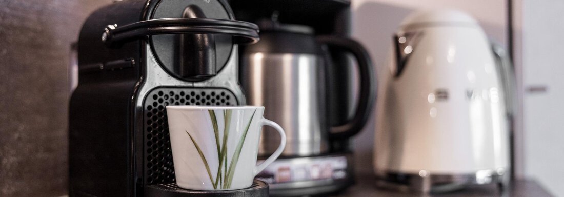 A modern coffee machine is on the countertop in a kitchen. Next to the machine is a white teapot. - MYALPS Himmelreich - Längenfeld