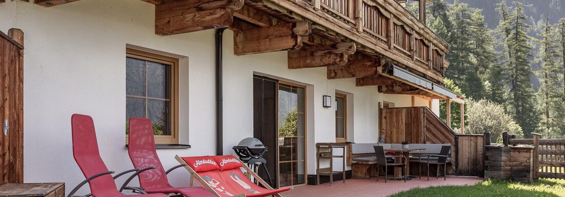 A cozy terrace with loungers and a dining area. In the background, mountains and trees are visible. - MYALPS Himmelreich - Längenfeld