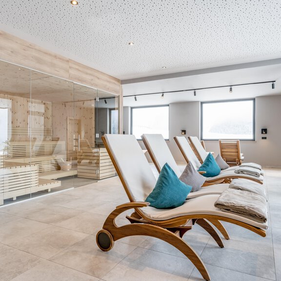 A modern wellness area with comfortable loungers and large windows. In the background, one can see a sauna and plants in decorative pots. - Nativo, Bergaparts-Genussplatz - Längenfeld