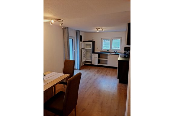 Essen und Kochen Eine moderne Küche mit einem Holztisch und zwei Stühlen. Der Raum ist hell und freundlich, mit einem großen Fenster und einem Kühlschrank. - Apart Stefan - Niederthai