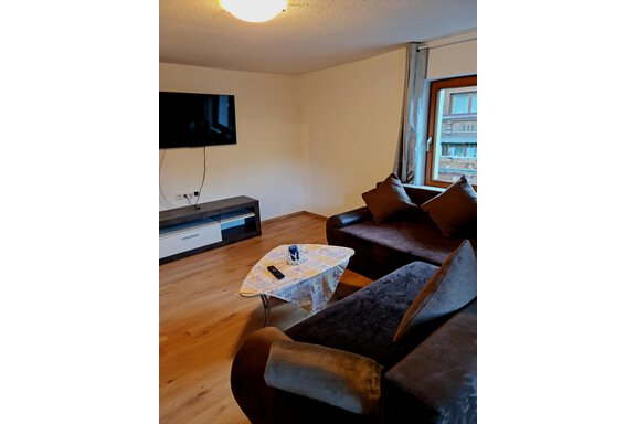 Ein gemütliches Wohnzimmer mit einer dunklen Couch und einem Tisch. An der Wand hängt ein Fernseher und ein Fenster sorgt für natürliches Licht. - Apart Stefan - Niederthai