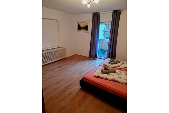 Ein gemütliches Schlafzimmer mit Holzfußboden und einem Balkon. Die Betten sind mit vielen Kissen und Decken dekoriert. - Apart Stefan - Niederthai