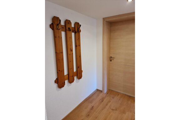 Ein Holzkleiderständer mit mehreren Haken an einer weißen Wand. Im Hintergrund ist eine Tür aus hellem Holz zu sehen. - Apart Stefan - Niederthai