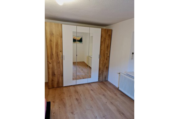 Ein moderner Kleiderschrank mit Spiegeln und Holzverkleidung steht in einem hellen Raum. Der Boden ist mit einem warmen Holzfußboden ausgestattet. - Apart Stefan - Niederthai