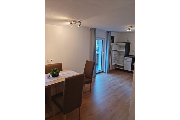 Ein helles Esszimmer mit einem Tisch und zwei Stühlen. Im Hintergrund ist eine offene Küche mit einem Kühlschrank sichtbar. - Apart Stefan - Niederthai