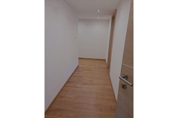 Ein heller Flur mit einem Holzfußboden. Die Wände sind weiß, und es gibt eine Tür auf der rechten Seite. - Apart Stefan - Niederthai