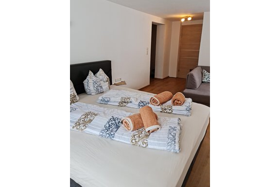 Ein gemütliches Schlafzimmer mit einem Doppelbett und einem beigen Bettbezug. Auf dem Bett liegen gefaltete Handtücher und in der Ecke steht ein Sofa. - Apart Stefan - Niederthai