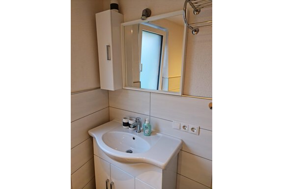 Ein modernes Badezimmer mit einem eleganten Waschbecken und Spiegel. An der Wand befinden sich helle Fliesen und einige Pflegeprodukte. - Apart Stefan - Niederthai