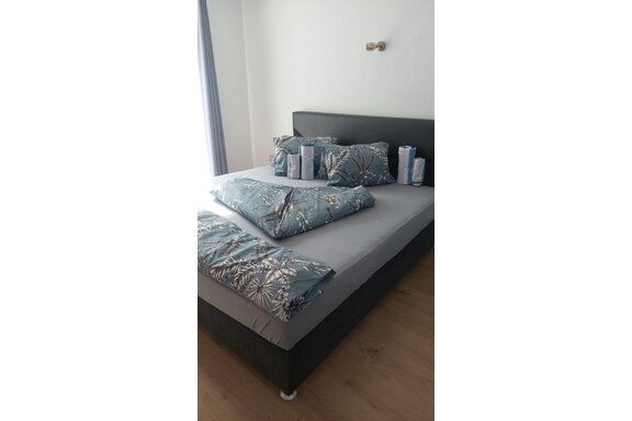 Ein modernes Schlafzimmer mit einem großen Bett und dekorativen Kissen in blau-grünen Tönen. Die Wände sind hell, und es gibt viel Tageslicht. - Apart Stefan - Niederthai