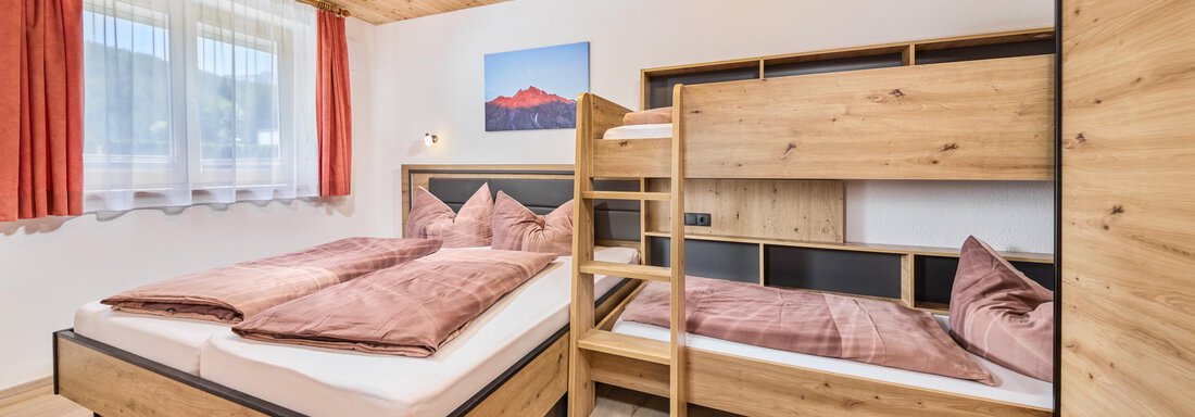 Schlafzimmer mit Etagenbett A cozy bedroom with a double bed and a bunk bed. The warm wooden furniture and the windows with curtains create an inviting atmosphere. - Appartement Lea - Niederthai