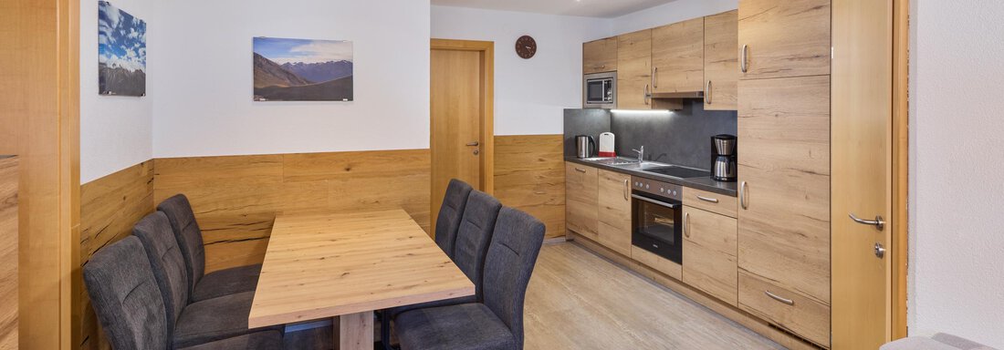 A cozy kitchen with a wooden dining area and modern appliances. The walls are in neutral colors and there are photos of mountains. - Appartement Lea - Niederthai
