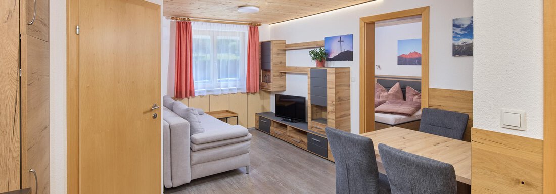 A modern living space with wooden paneling and a cozy sofa. The room features a dining area with chairs and decorative pictures on the wall. - Appartement Lea - Niederthai
