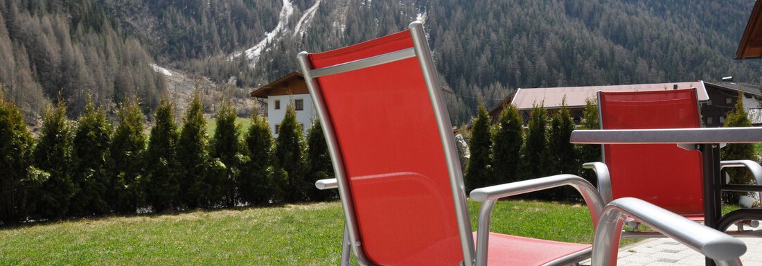 Eine ruhige Terrasse mit Gartenmöbeln, umgeben von grünen Pflanzen. Im Hintergrund sind majestätische Berge zu sehen. - Appartement Leiter Niki - Niederthai