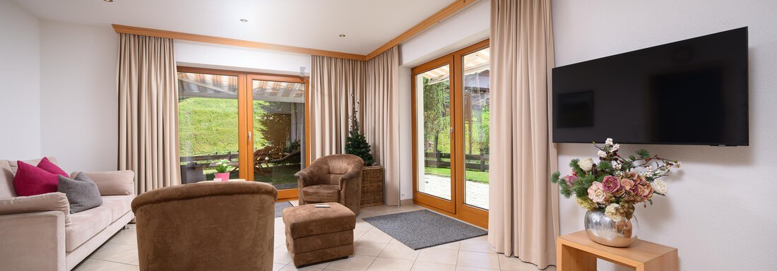 A cozy living space with comfortable armchairs and a sofa bed. Large windows offer a view of the green surroundings. - Delano Appartements - Niederthai