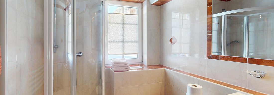 Ein modernes Bad mit einer Dusche, einem WC und einem Waschbecken. Helle Fliesen und Holzdetails sorgen für eine einladende Atmosphäre. - Gipfelblick Appartements - Niederthai