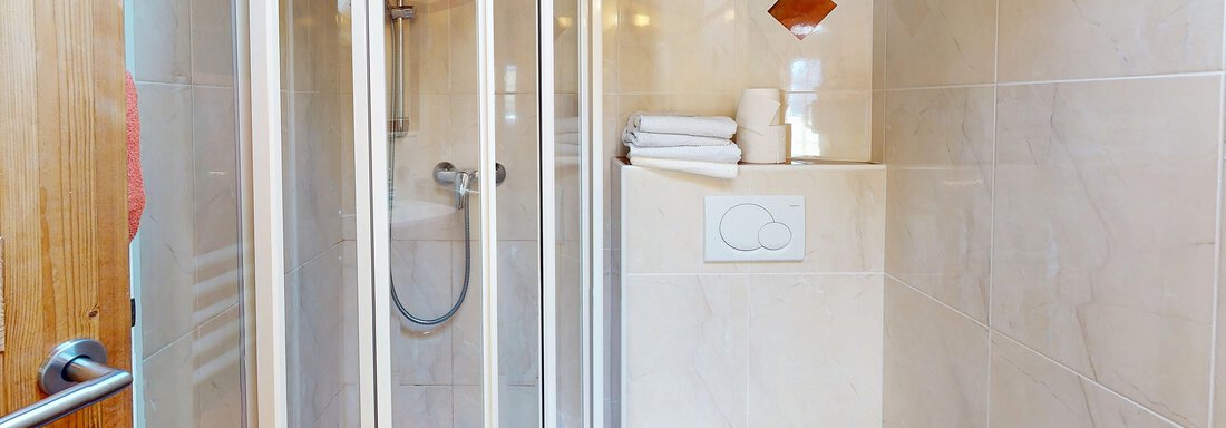 Ein modernes Badezimmer mit einer Dusche und einer sanitären Einrichtung. Die Wände sind hell gefliest und es gibt frische Handtücher. - Gipfelblick Appartements - Niederthai