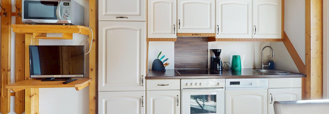 Eine moderne Küche mit hellen Schränken und einer Holzverkleidung. Die Ausstattung umfasst eine Mikrowelle, einen Fernseher und einen Kaffeeautomaten. - Gipfelblick Appartements - Niederthai