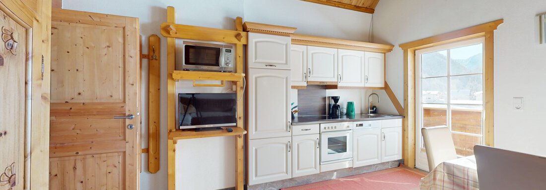 Eine gemütliche Küche mit Holzregalen und modernen Geräten. Der Raum hat viel Licht durch große Fenster und eine warme Atmosphäre. - Gipfelblick Appartements - Niederthai