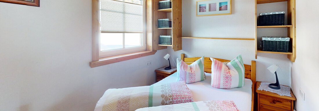 Ein gemütliches Schlafzimmer mit zwei separaten Betten und bunten Kissen. Der Raum ist hell und modern eingerichtet, mit einem Fenster und Regalen an der Wand. - Gipfelblick Appartements - Niederthai