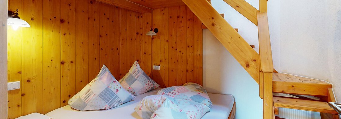 Ein gemütliches Schlafzimmer mit Holzwänden und einem Etagenbett. Die Inneneinrichtung ist einfach und einladend, mit Kissen auf dem Bett und einer Holztreppe. - Gipfelblick Appartements - Niederthai