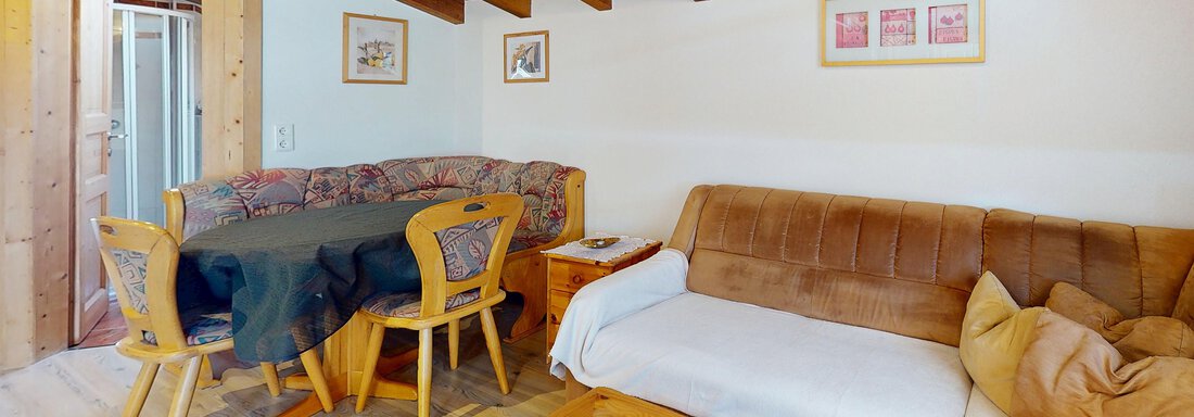 Ein gemütlicher Wohnraum mit Holzbalkendecke. Es gibt ein Sofa, einen Tisch und einige Stühle, die eine einladende Atmosphäre schaffen. - Gipfelblick Appartements - Niederthai
