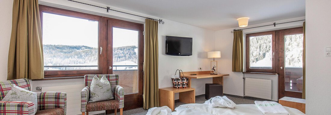 Ein gemütliches Hotelzimmer mit zwei bequemen Sesseln und großen Fenstern, die den Blick auf die Berge freigeben. Die Einrichtung ist modern und einladend. - Hotel Falknerhof, am Ursprung - Niederthai