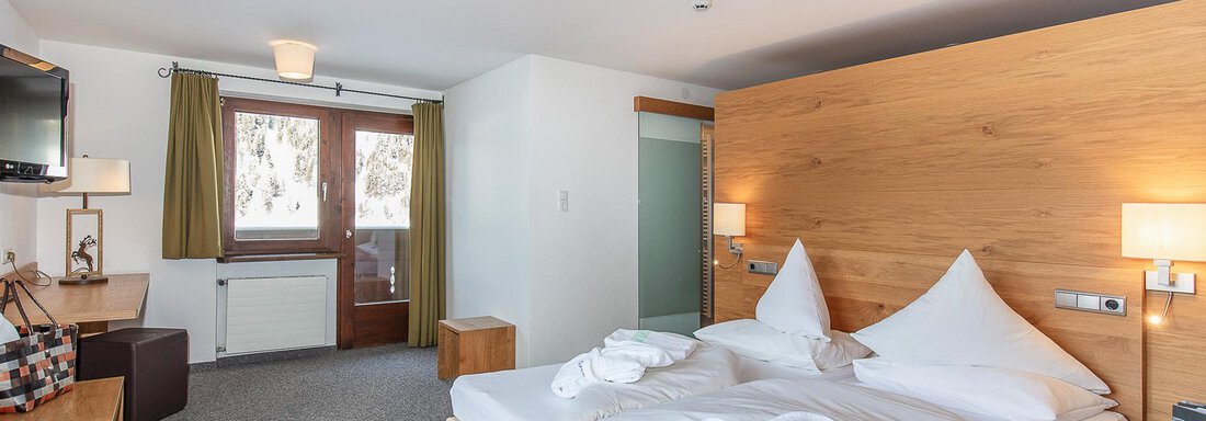 Ein modernes Hotelzimmer mit einem Doppelbett und zwei Kopfkissen. Große Fenster sorgen für viel Tageslicht und eine gemütliche Atmosphäre. - Hotel Falknerhof, am Ursprung - Niederthai