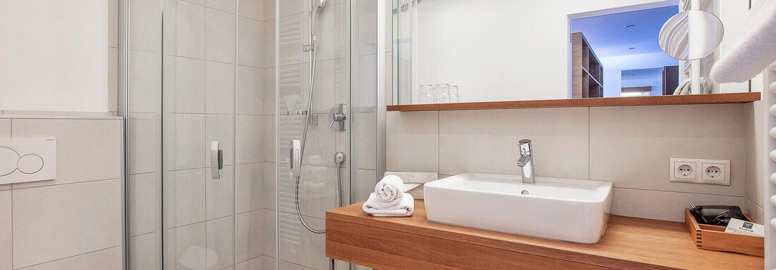 Ein modernes Badezimmer mit einer Glasdusche und einem Waschtisch aus Holz. Die Wände sind hell und gut beleuchtet. - Hotel Falknerhof, am Ursprung - Niederthai