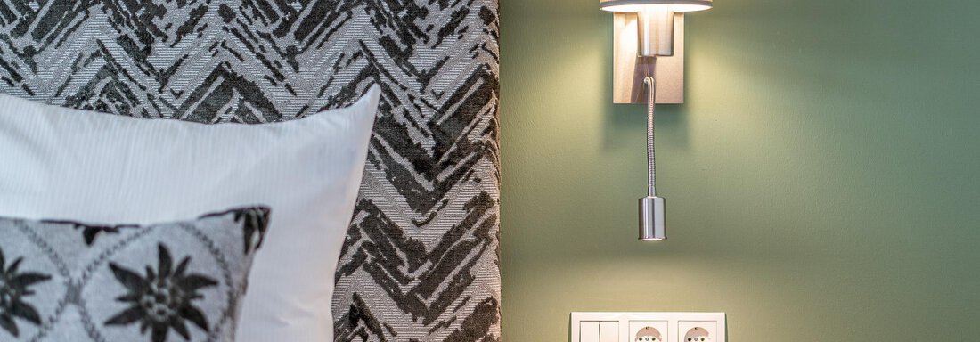 Ein modernes Schlafzimmer mit einem stilvollen Kopfteil und einem Leseleuchten an der Wand. Die sanfte Wandfarbe und die Kissen verleihen dem Raum eine einladende Atmosphäre. - Hotel Falknerhof, am Ursprung - Niederthai