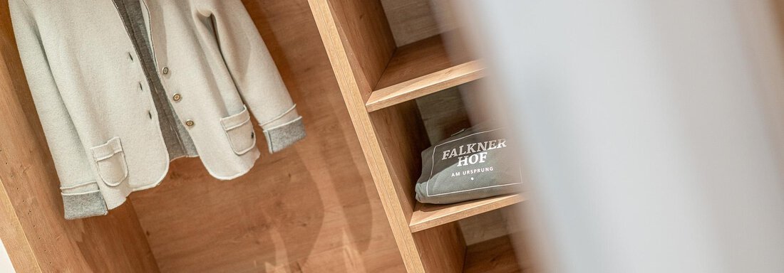 Ein Kleiderschrank aus Holz mit einem weißen Blazer und einem grauen Sweatshirt. Auf den Regalen liegen eine Tragetasche und ein paar Accessoires. - Hotel Falknerhof, am Ursprung - Niederthai