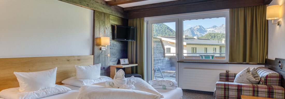 Ein modernes Hotelzimmer mit einem großen Bett und einem gemütlichen Sessel. Große Fenster bieten Blick auf die Berge draußen. - Hotel Falknerhof, am Ursprung - Niederthai