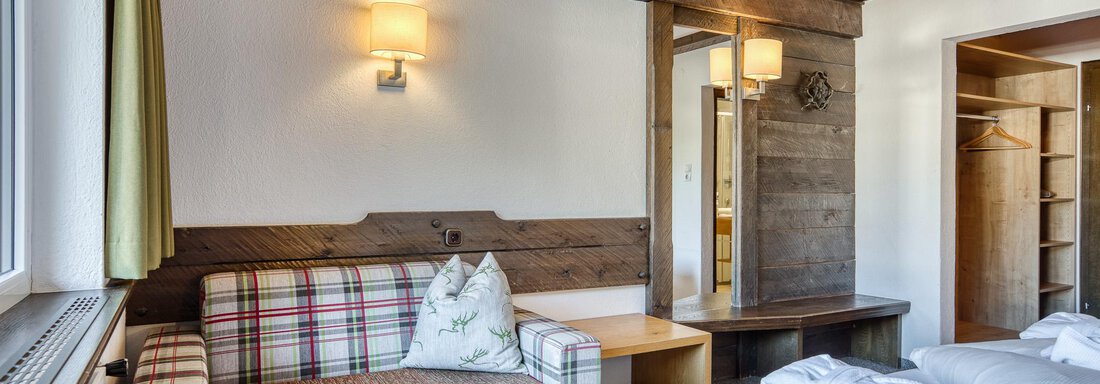 Ein gemütliches Zimmer mit Holzdecke und einem karierten Sofa. Es gibt ein Bett mit frischen Handtüchern und einen Spiegel im Raum. - Hotel Falknerhof, am Ursprung - Niederthai
