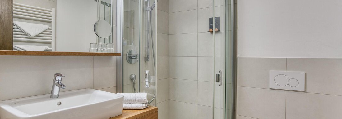 Ein modernes Badezimmer mit einer Dusche, einem Waschbecken und einem WC. Die Wände sind hell gefliest und es gibt viel Licht. - Hotel Falknerhof, am Ursprung - Niederthai