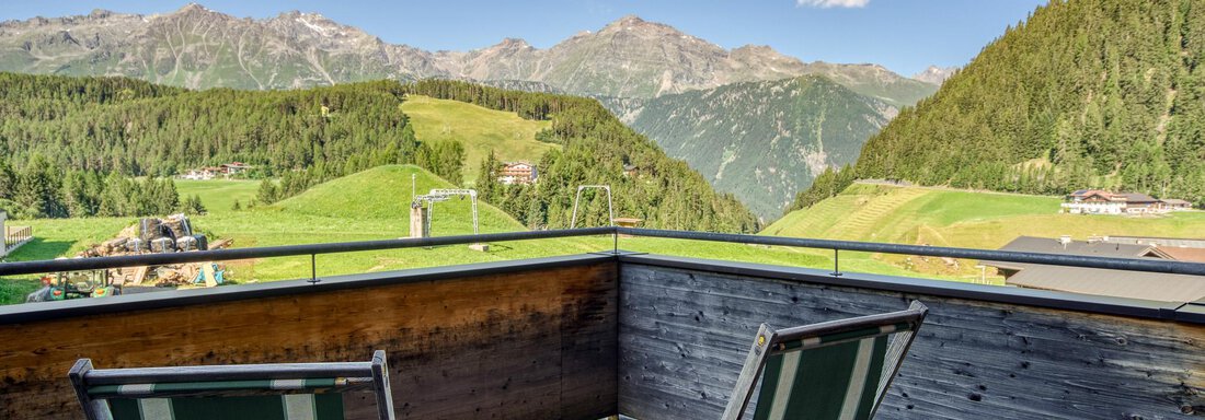 Ein Balkon mit zwei Liegestühlen und einem atemberaubenden Blick auf die grünen Berge. Der Himmel ist klar und sonnig. - Hotel Falknerhof, am Ursprung - Niederthai