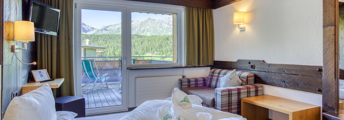 Ein gemütliches Zimmer mit einem großen Fenster und Blick auf die Natur. Es gibt ein bequemes Bett und eine Sitzecke mit modernem Design. - Hotel Falknerhof, am Ursprung - Niederthai