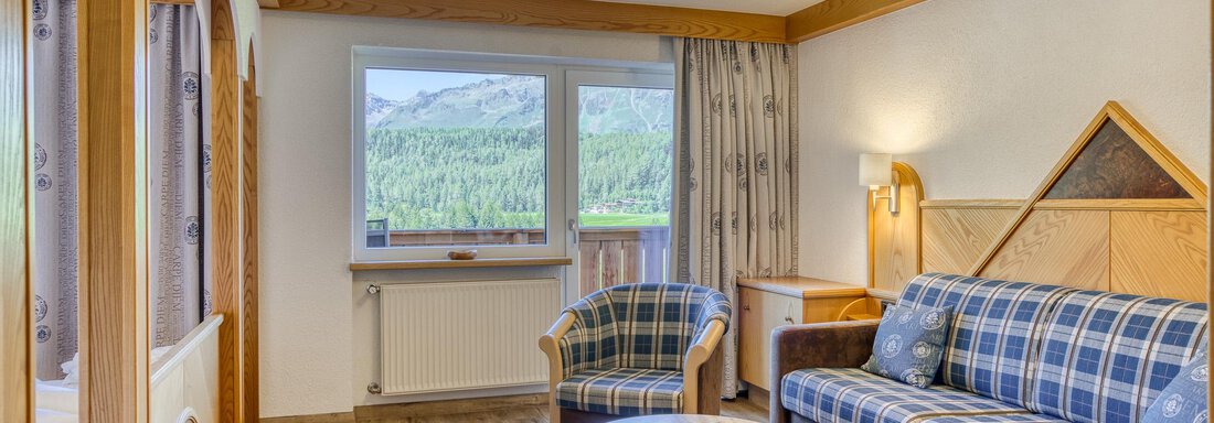 Ein gemütliches Wohnzimmer mit einem Sofa und einem Tisch. Große Fenster bieten einen Blick auf die umliegenden Berge. - Hotel Falknerhof, am Ursprung - Niederthai