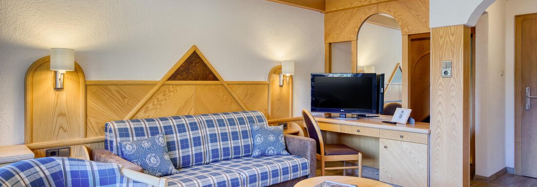 Ein gemütlicher Wohnraum mit einem blauen Sofa, einem Holztisch und einem Fernseher. Die Wände sind hell und es gibt eine warme Holzverkleidung. - Hotel Falknerhof, am Ursprung - Niederthai