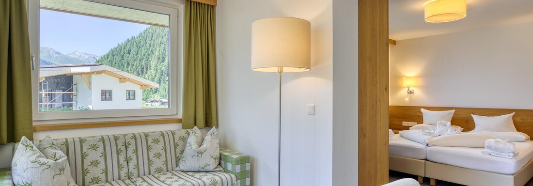 Ein gemütliches Zimmer mit einem modernen Sofa und einem Tisch. Im Hintergrund ist ein separater Schlafbereich mit einem Doppelbett zu sehen. - Hotel Falknerhof, am Ursprung - Niederthai