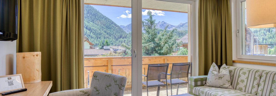 Ein helles Wohnzimmer mit einem Sofa und zwei Sessel. Große Fenster bieten Blick auf die Berge und die Terrasse. - Hotel Falknerhof, am Ursprung - Niederthai