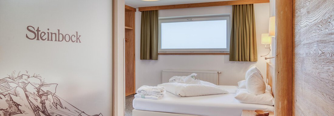 Ein gemütliches Hotelzimmer mit einem großen Bett und dekorativen Kissen. Durch das Fenster fällt Tageslicht, und die Wände sind in neutralen Tönen gehalten. - Hotel Falknerhof, am Ursprung - Niederthai